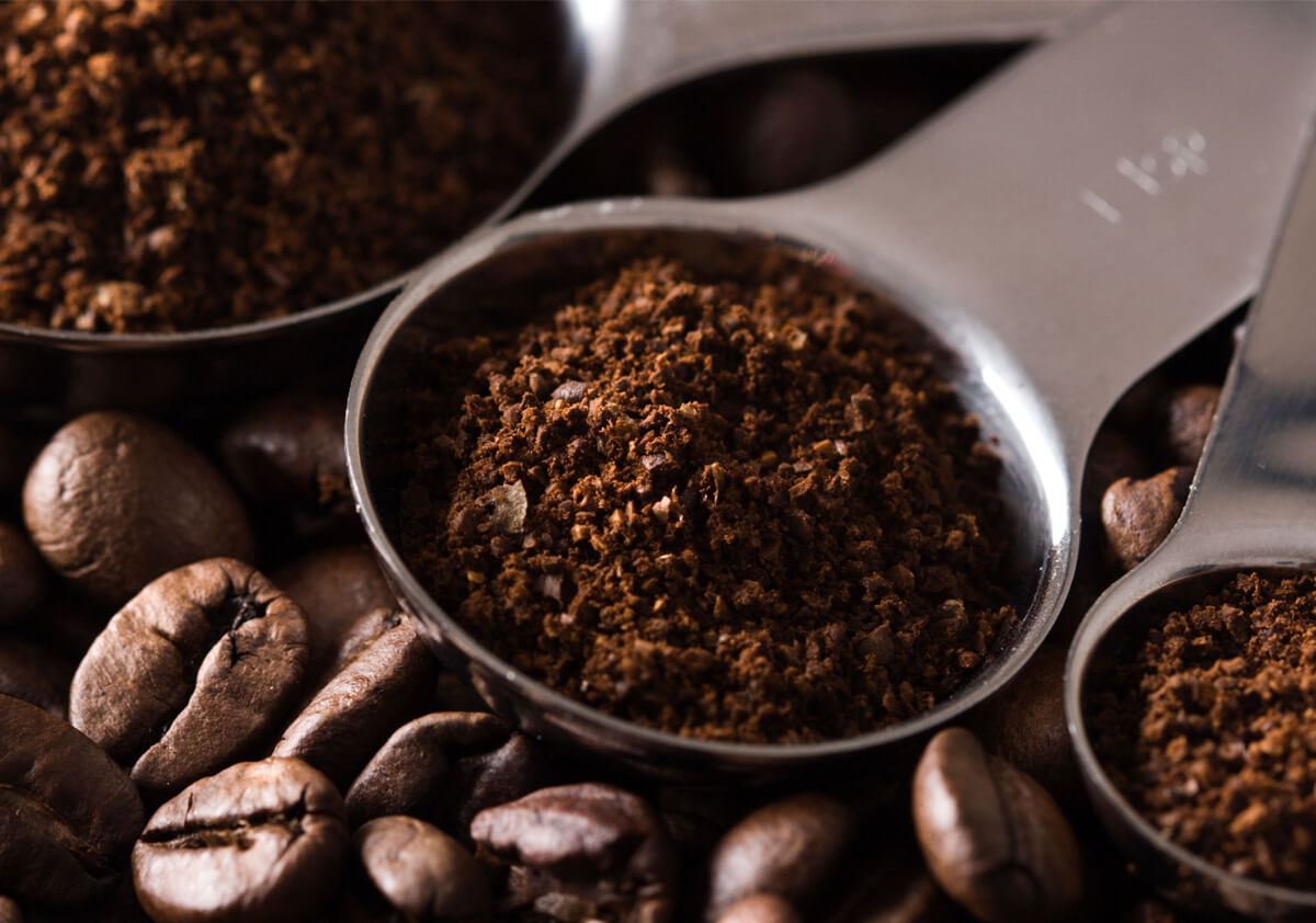 Measuring spoon with ground coffee surrounded by coffee beans